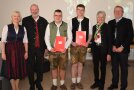 Junge Männer in Tracht mit Zeugnissen inder Hand, daneben Gratulanten.