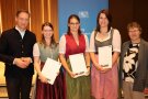 Drei Frauen in Dirndl mit Zeugnissen in den Händen, links ein Herr im Anzug, rechts steht eine Dame