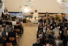 Blick auf sitzendes Publikum im Saal, vorne Geistliche im Messgewand.