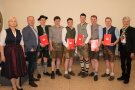 Junge Männer in Tracht mit Zeugnissen inder Hand, daneben Gratulanten.