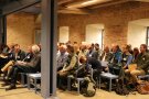 Interessierte Zuhörer sitzen in einem historischen Saal.