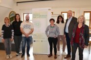 Sieben Personen stehen rechts und links von informativem Roll-up.