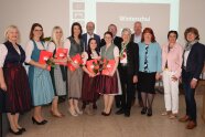 Gruppe von jüngeren Frauen in Tracht mit Zeugnissen in der Hand, links und rechts daneben Gratulanten.