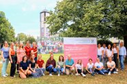 Gruppe von Frauen in Grünanlage mit großem Plakat zum Tag der offenen Tür.