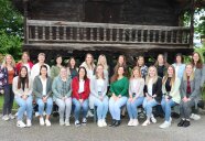 Frauen in zwei Reihen stehen und Sitzen für ein Gruppenbild vor einer Holzhütte beisammen.