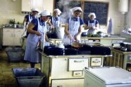 Historisches Bild der Schulküche, fünf Frauen mit Schürzen und Häubchen sind am Kochen.