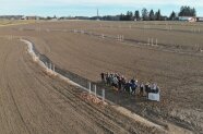 Luftbild von Personengruppe steht mit Schaufeln und Spaten an einem Graben auf dem Acker.