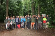 Große Gruppe von Personen in mehreren Reihen präsentiert sich im Wald für ein Gruppenbild.