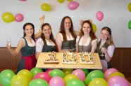 Fünf Frauen in Tracht mit Geburstagskuchen in Form der Zahlen 100 und bunten Luftballons drumherum