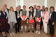 Gruppe von jungen Männern in Tracht mit Zeugnissen in der Hand, links und rechts daneben Gratulanten.