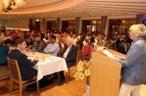 Publikum sitzt in Festsaal, rechts Frau an Rednerpult.