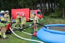 Feuerwehrleute bauen blaues Wasserbecken auf und hantieren mit Schläuchen.