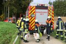 Feuerwehrauto an Waldrand, Feuerwehrleute mit Ausrüstung tragen aufgewickelte Schläuche.