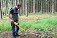 Mann sucht mit Sonde den Waldboden ab.