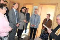 Personengruppe in Holzgebäude, rechts Pfarrer bei Segnung.