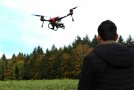 Mann mit Steuerung fliegt Drohne über das Feld.