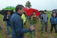 Landwirt mit Pflanzen in der Hand auf Feld vor Zuhörern