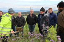 Gruppe von Personen in Feld, Mann nimmt mit Spaten Probe.