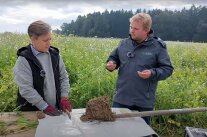 Mann und Frau im Feld mit einem mit Erdreich bedeckten Spaten.